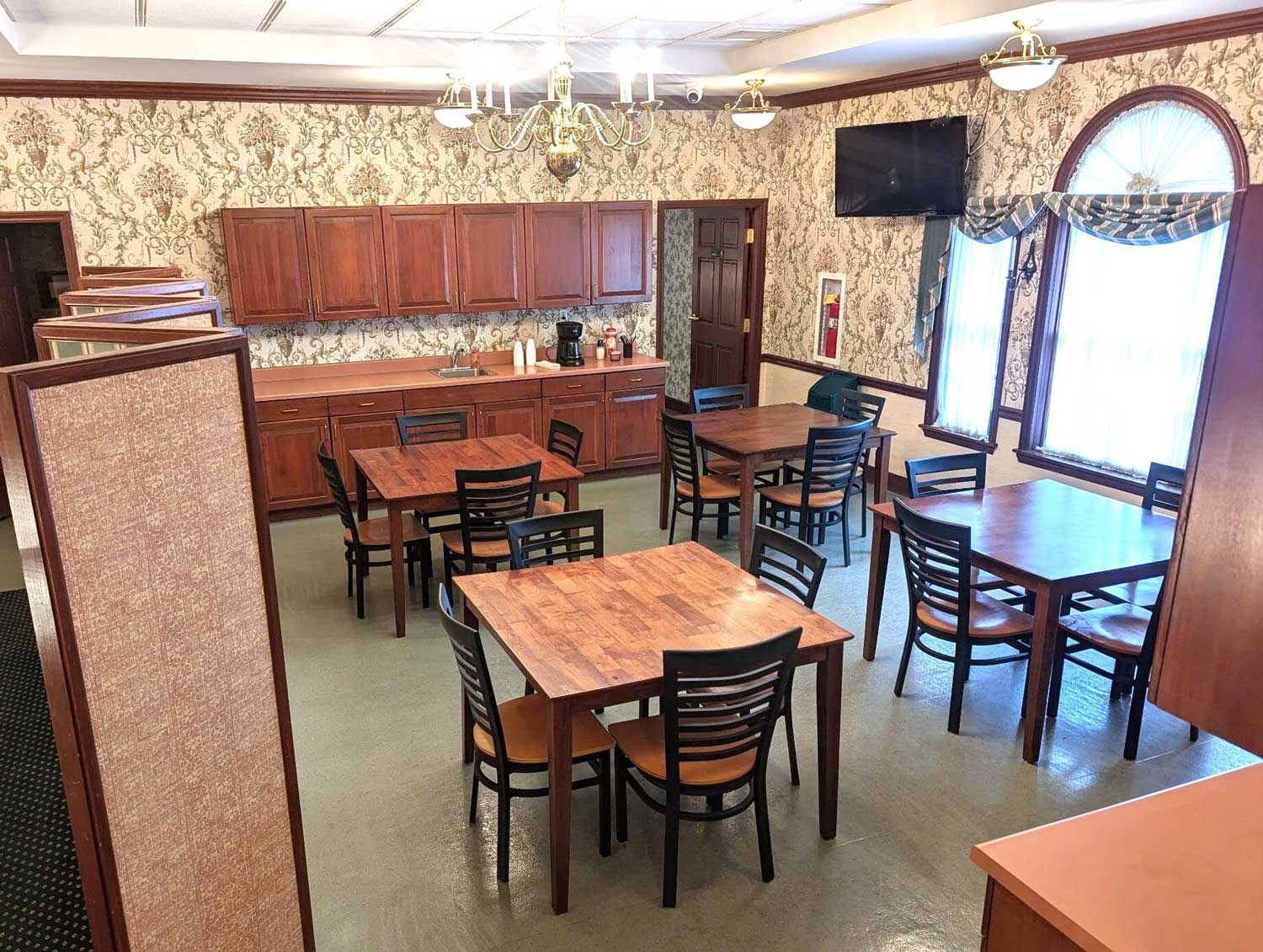 Neatly arranged wooden chairs and tables featuring wooden shelves and a wall-mounted tv inside the lounge area.